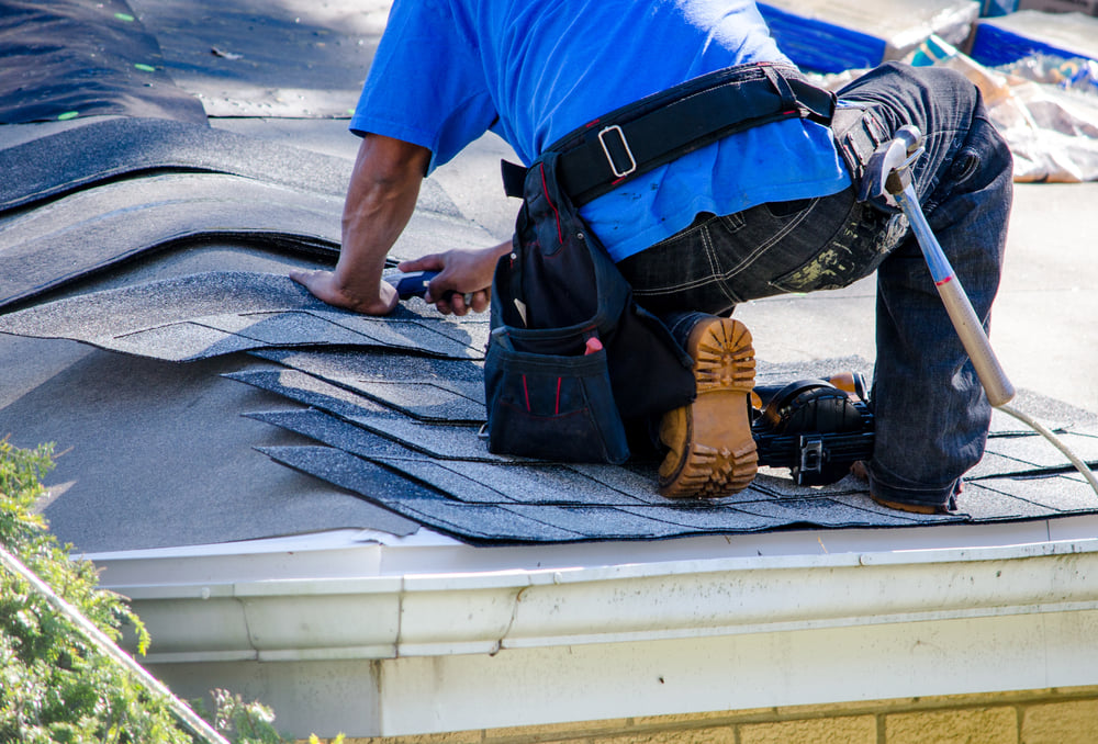Roofer trims asphalt shingles being installed on a house. Roofing & Siding Specialist Inc