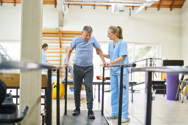 Man walks at the parallel bars for stability while he works with physiotherapist to build strength and mobility.