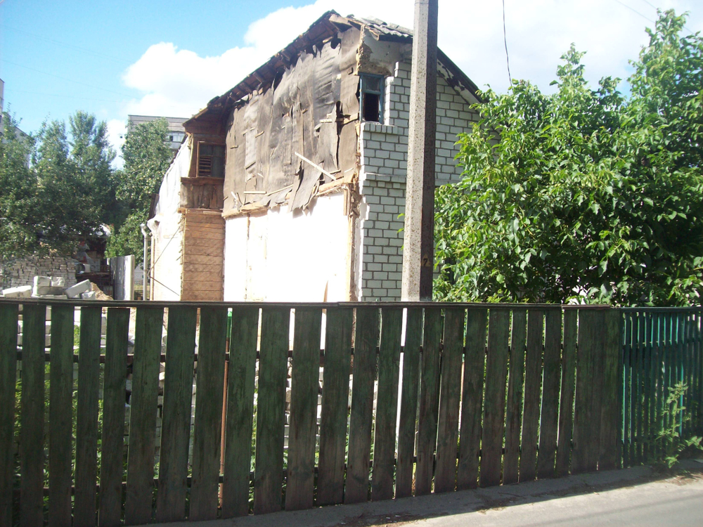 Modern Remodeling worksite with partially demolished brick house and new construction materials behind a wooden fence