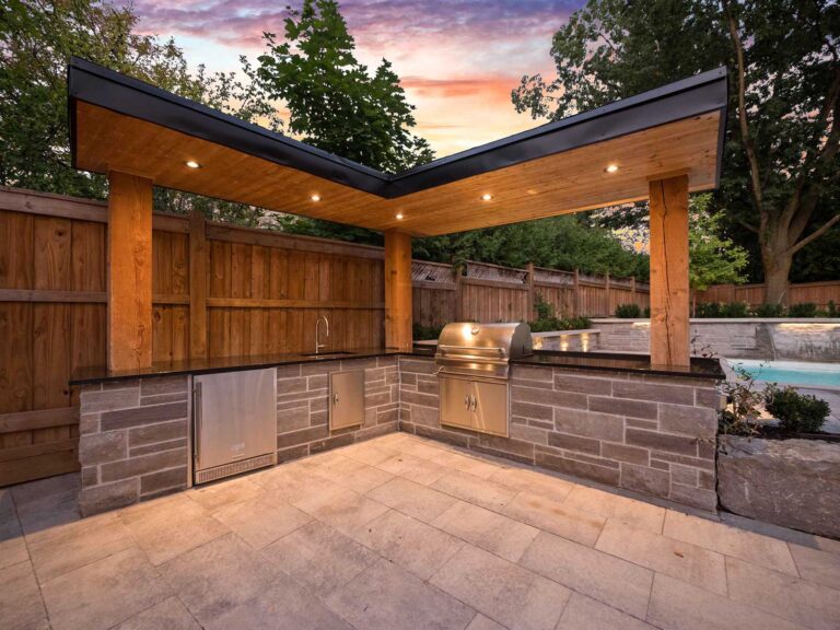 Outdoor kitchen with stone bar, luxury grill, black countertops and sink, large wood pillars hold roof overhang