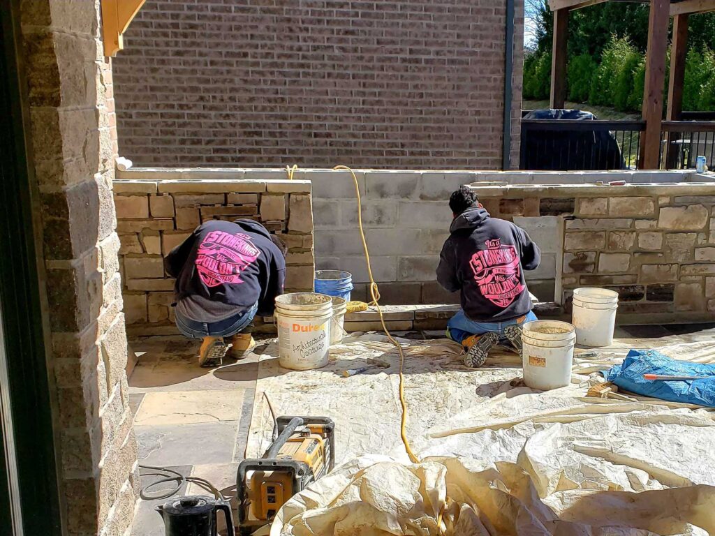 Stoneworkers install veneer around a concrete base for beautiful stone wall.