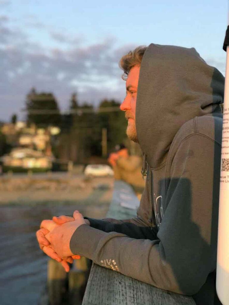 Anchor Hearing team member listening outdoors by the water, wearing a hoodie and using hearing assistance technology