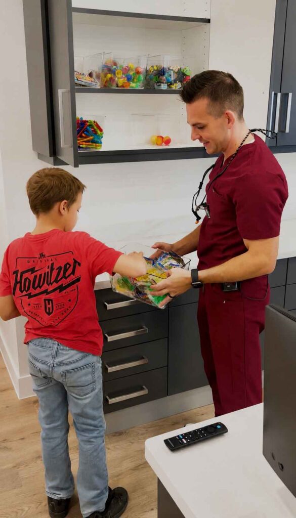 Pediatric dentist Johnson Pediatric Dentistry helping a child at the reception desk with a gift bag in a dental clinic