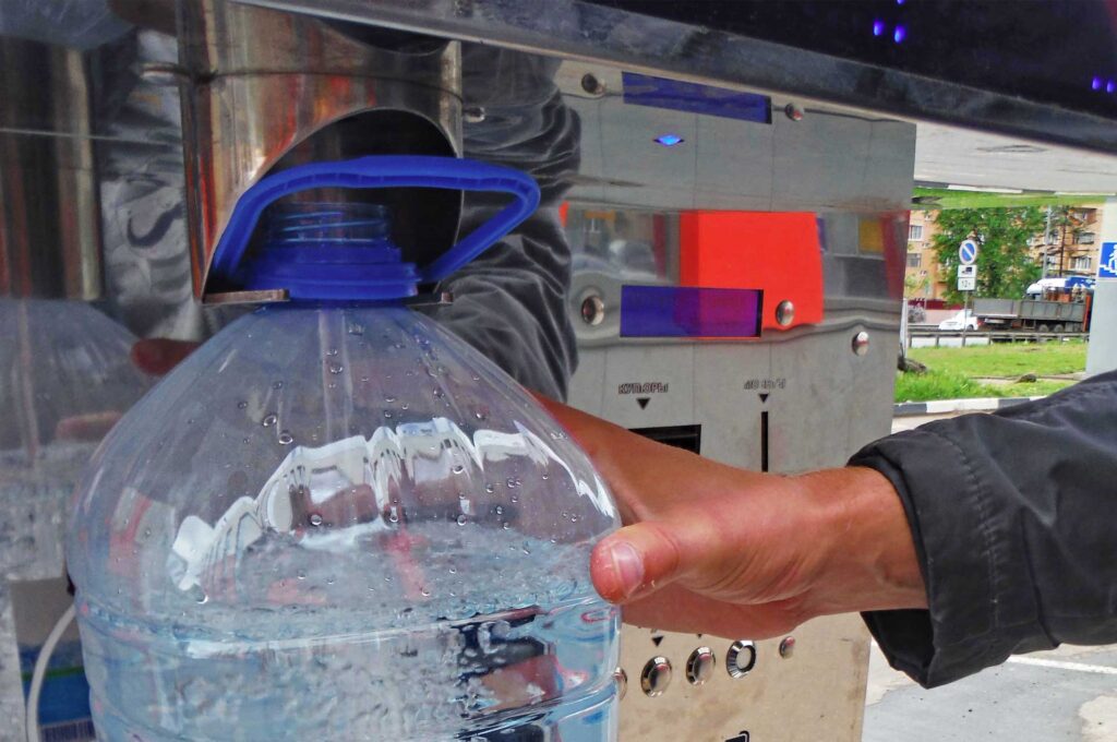 A man pours water into a bottle from an outdoor water dispenser
