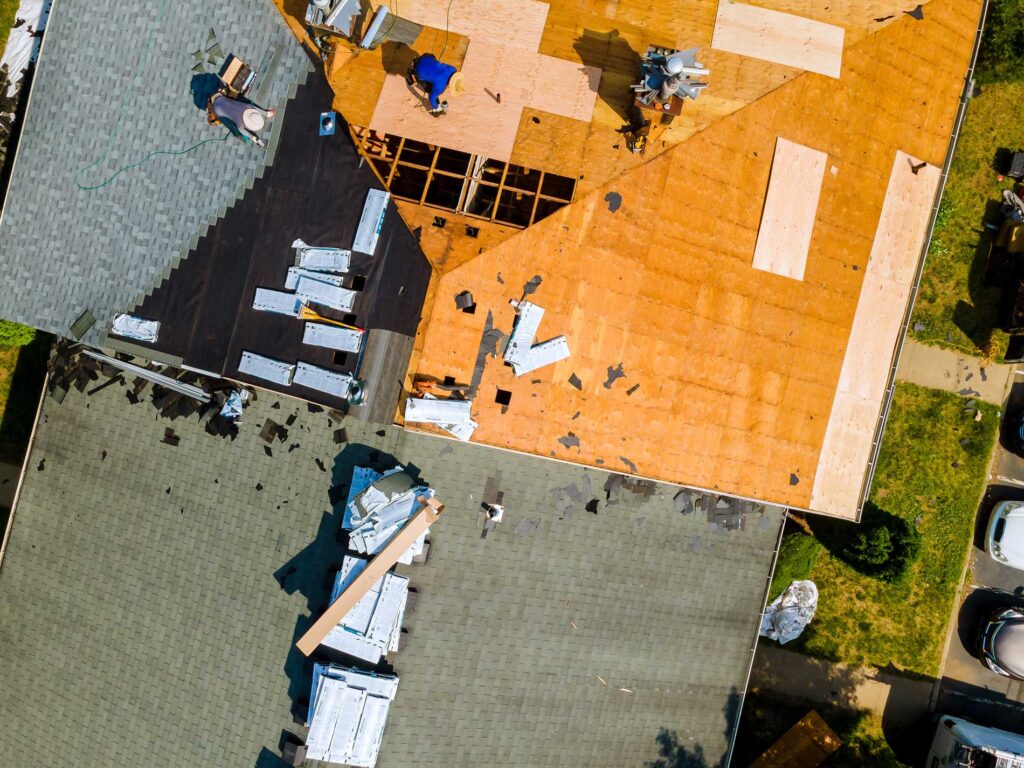 Aerial view of JN Roofing workers installing shingles on a residential roof deck with materials and tools