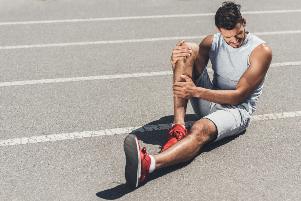 Man holding his injured knee while sitting on the pavement, representing pain and sports injury coverage