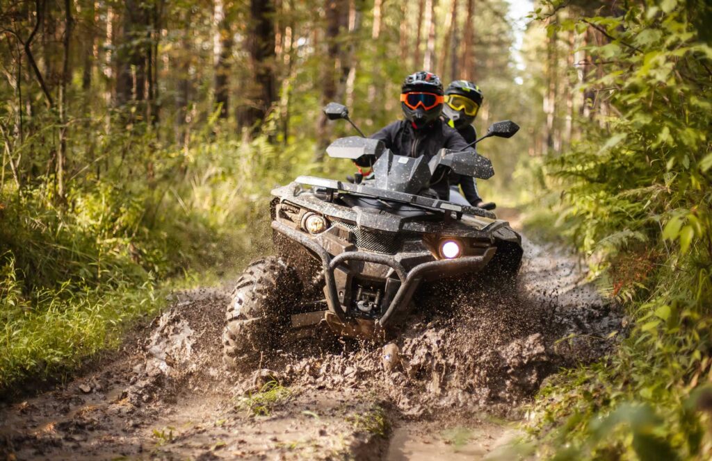 Off-road ATV riders splashing through a muddy trail in the woods
