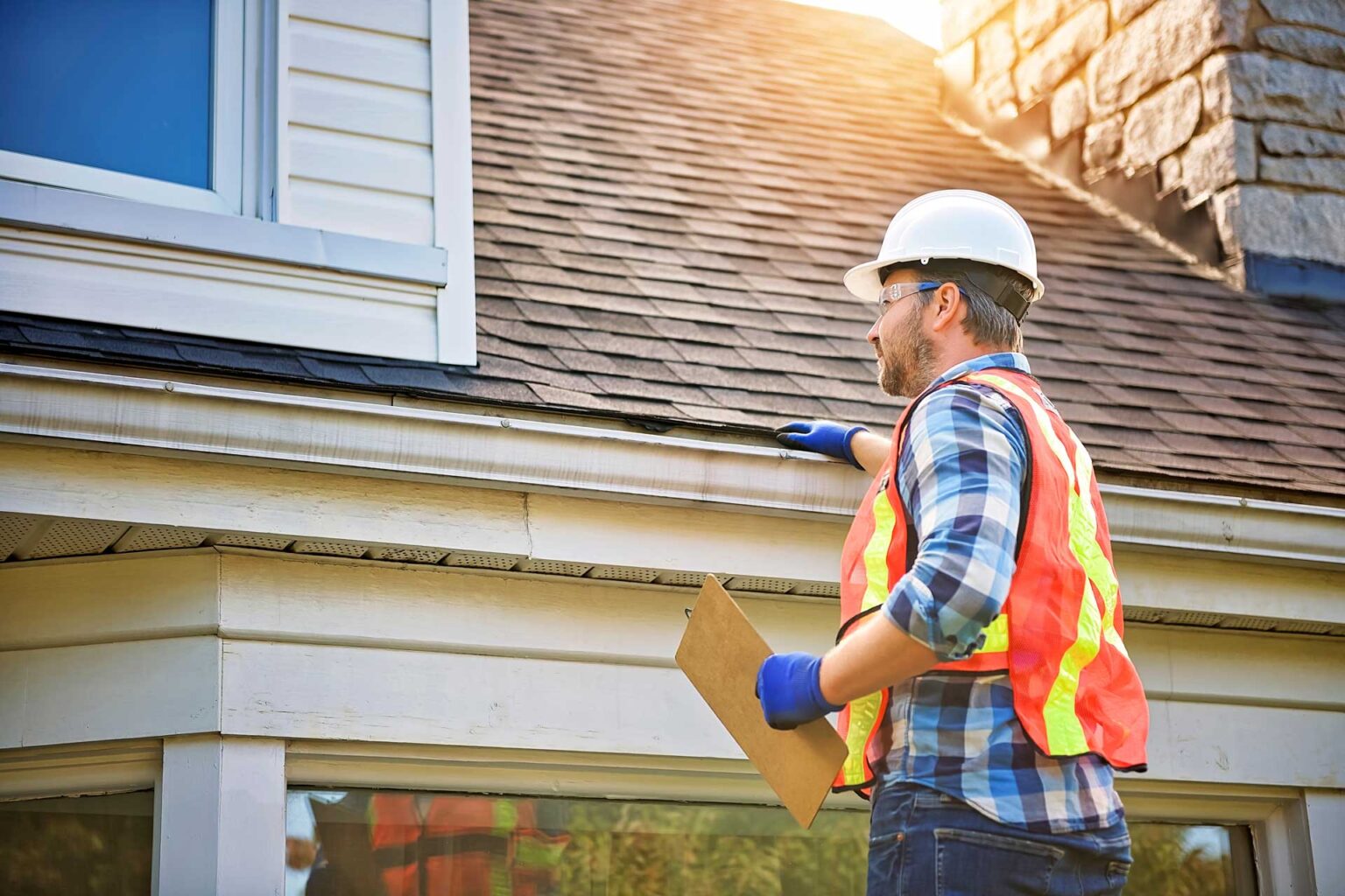 A man with hard hat standing on steps inspecting house roof