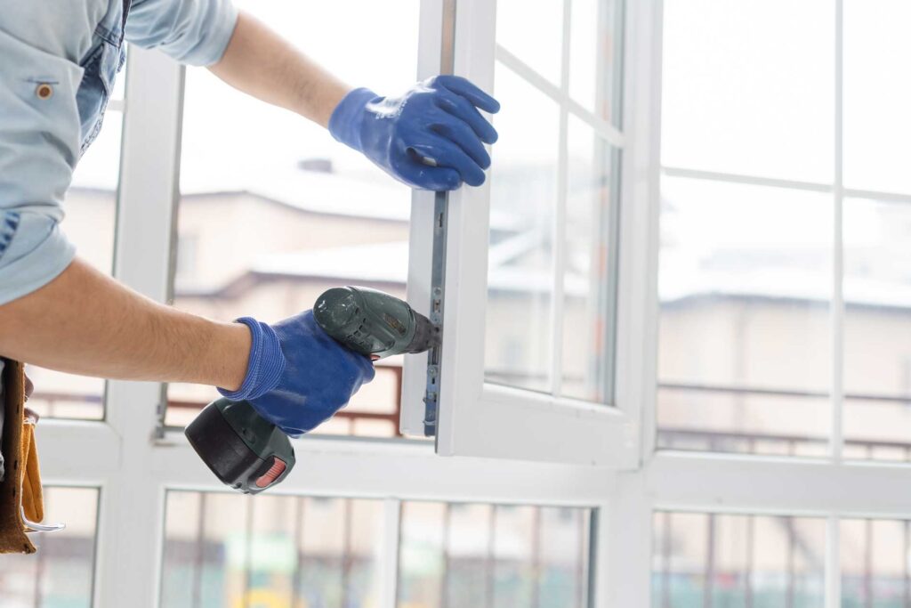 Technician installing a glass window for Mid Coast Glass wearing gloves and using a drill