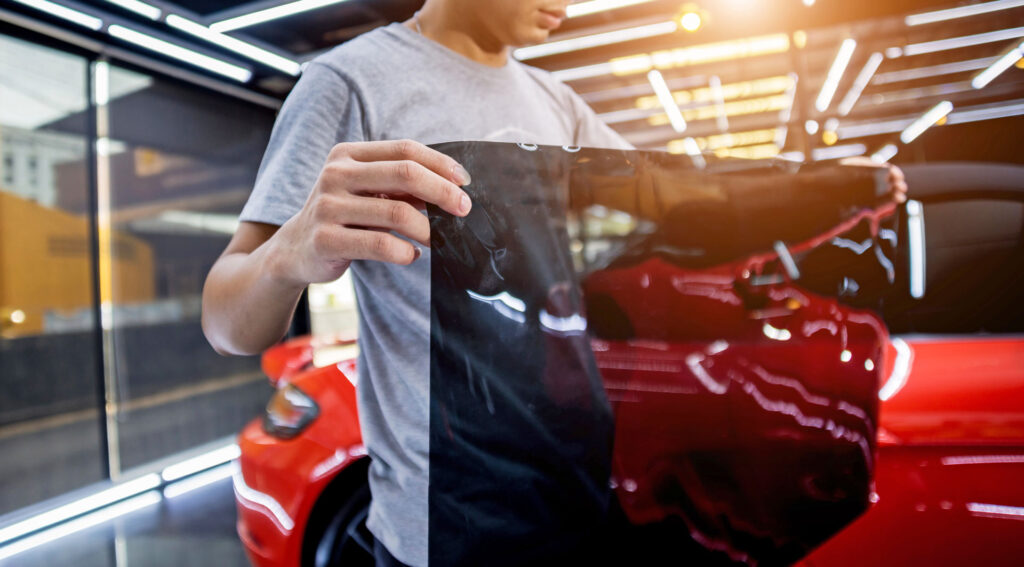 Mobile window tinting technician applying car window tint film to vehicle