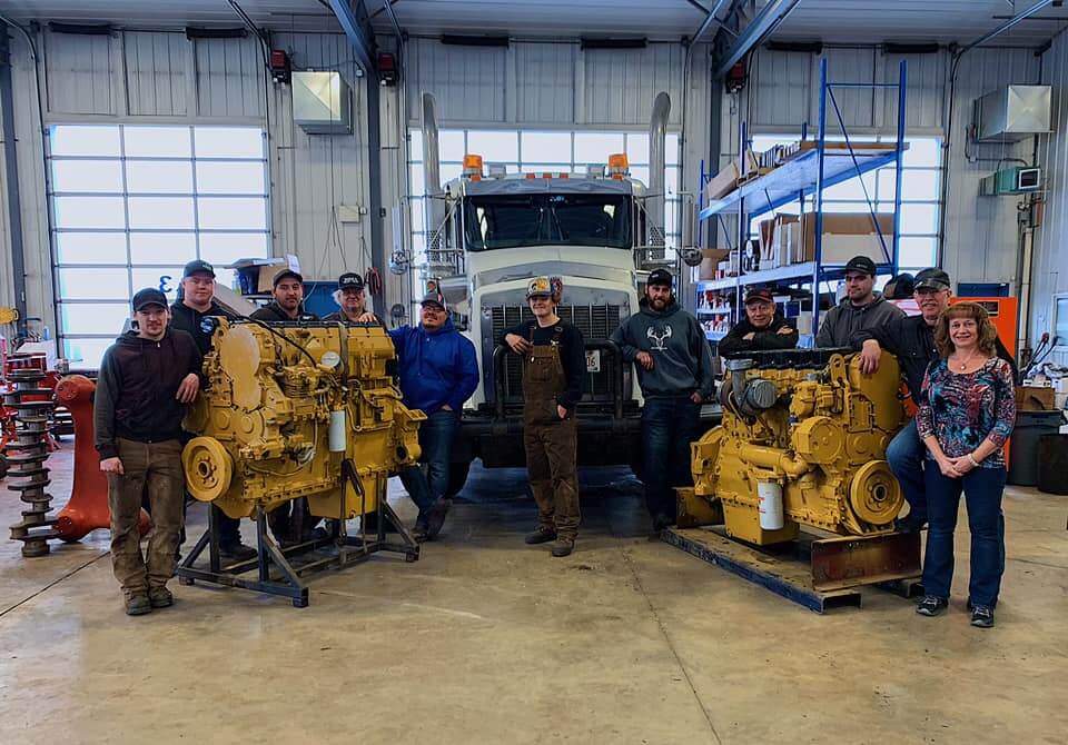 KJ's Repair Service Ltd team standing in workshop with heavy machinery and engines on display