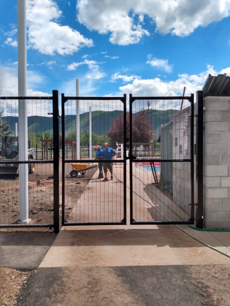 Alpine Fencing & Supplies Inc. installation of a black metal fence with gates and posts under a blue sky