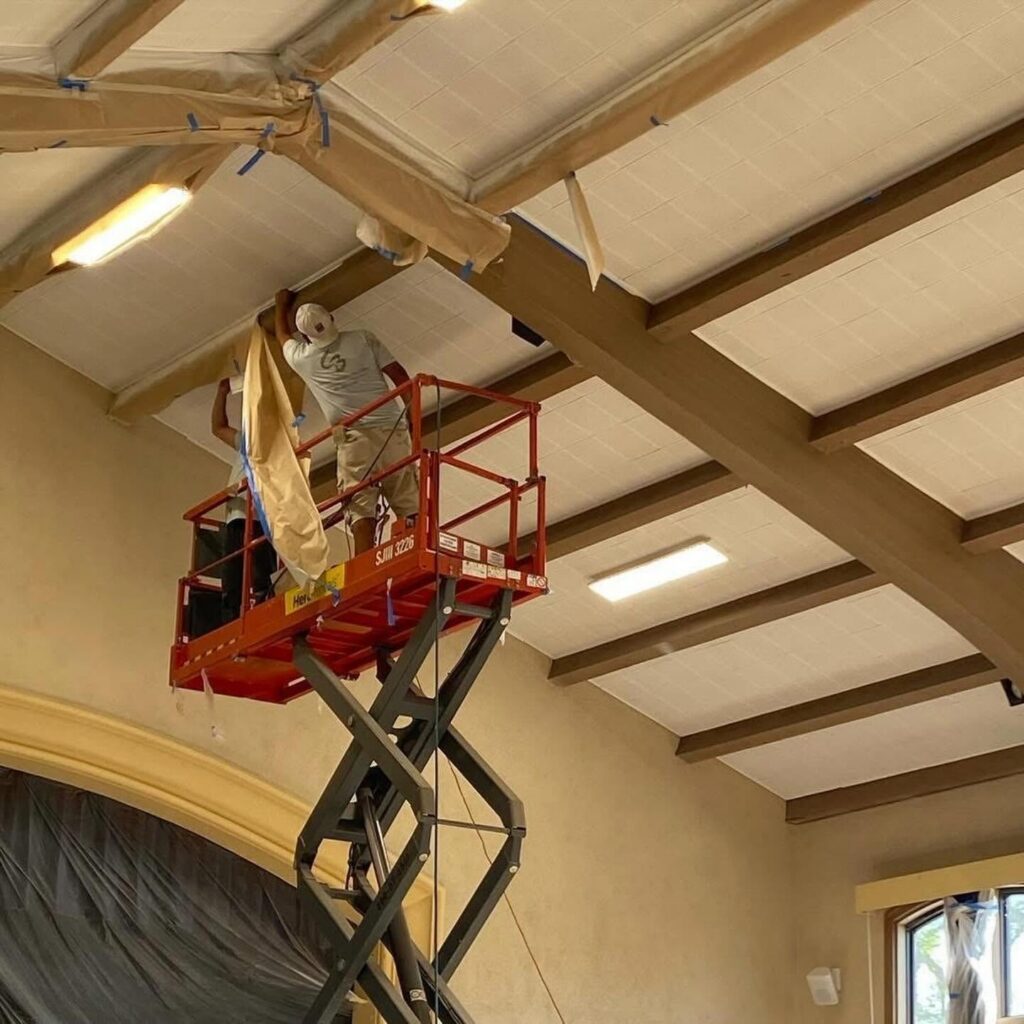 CB Paint & Decor painter using scaffolding to apply paint on ceiling and beams indoors