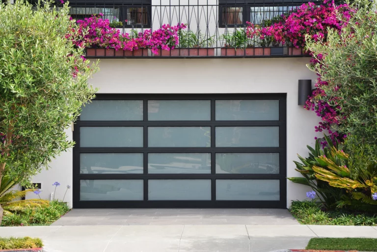 Glass Modern Garage door on Stucco home with surrounding landscaping. Patio above garage.