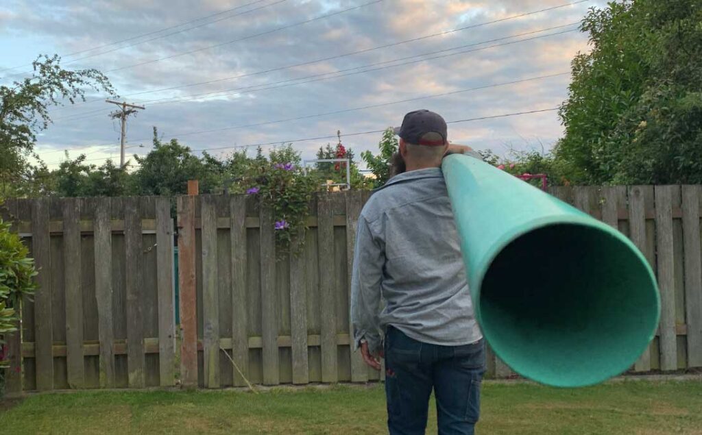 Skagit Sewer Specialists technician holding a large sewer pipe in a backyard