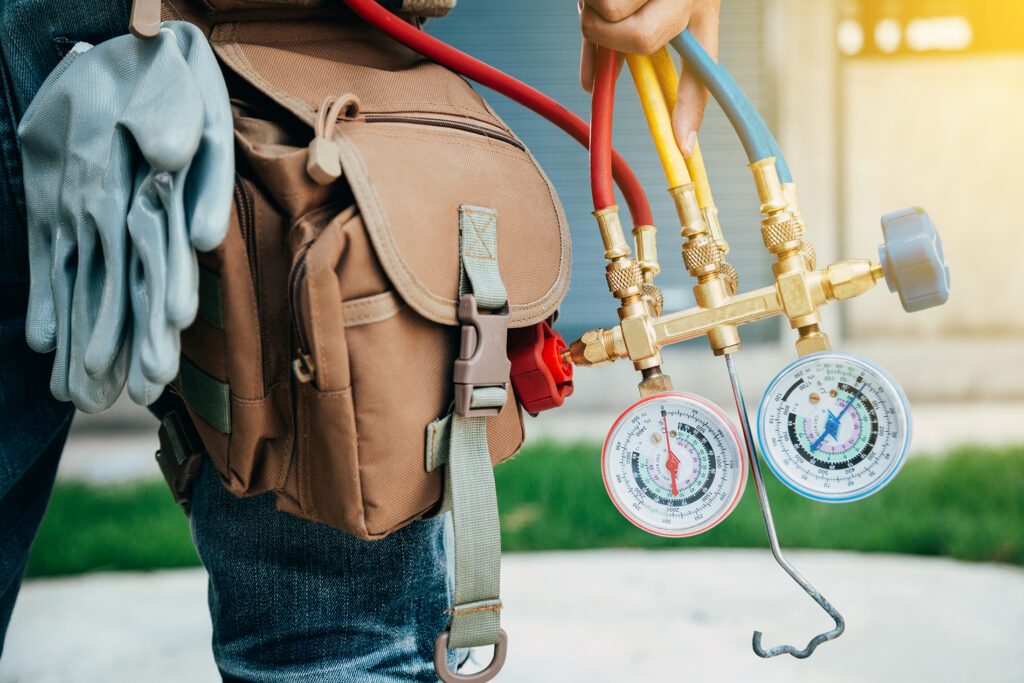 Close-up of HVAC refrigerant manifold gauges and hoses hanging from a technician's tool bag