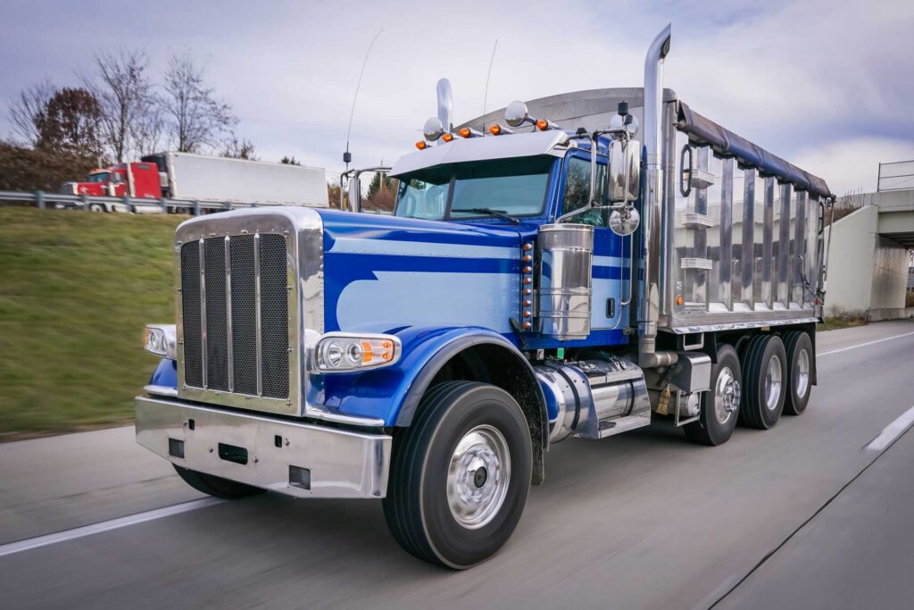 Blue semi truck hauling a dump trailer driving on a highway