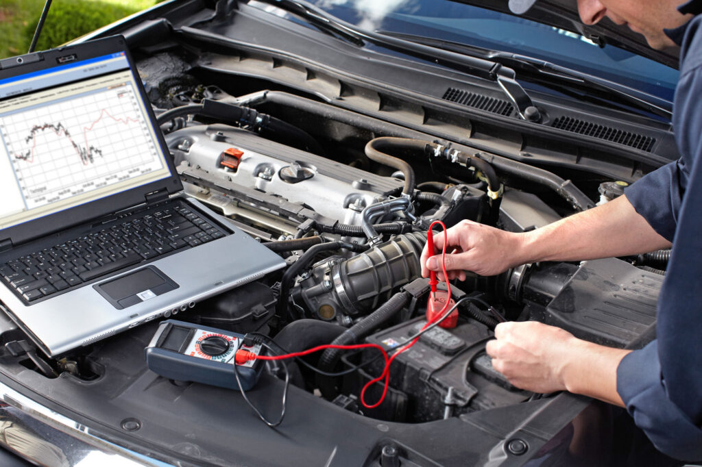 All America Brake and Spring Mechanic running a computer diagnostic test on a car engine using a laptop