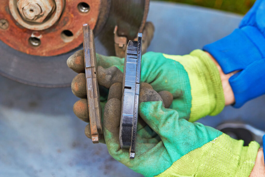 Gloved hand holding a worn brake pad for inspection