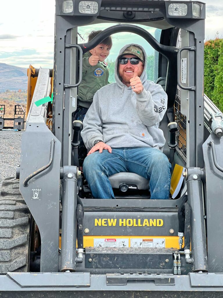 Wamsley Well Drilling team member and child smiling while seated in a drilling rig