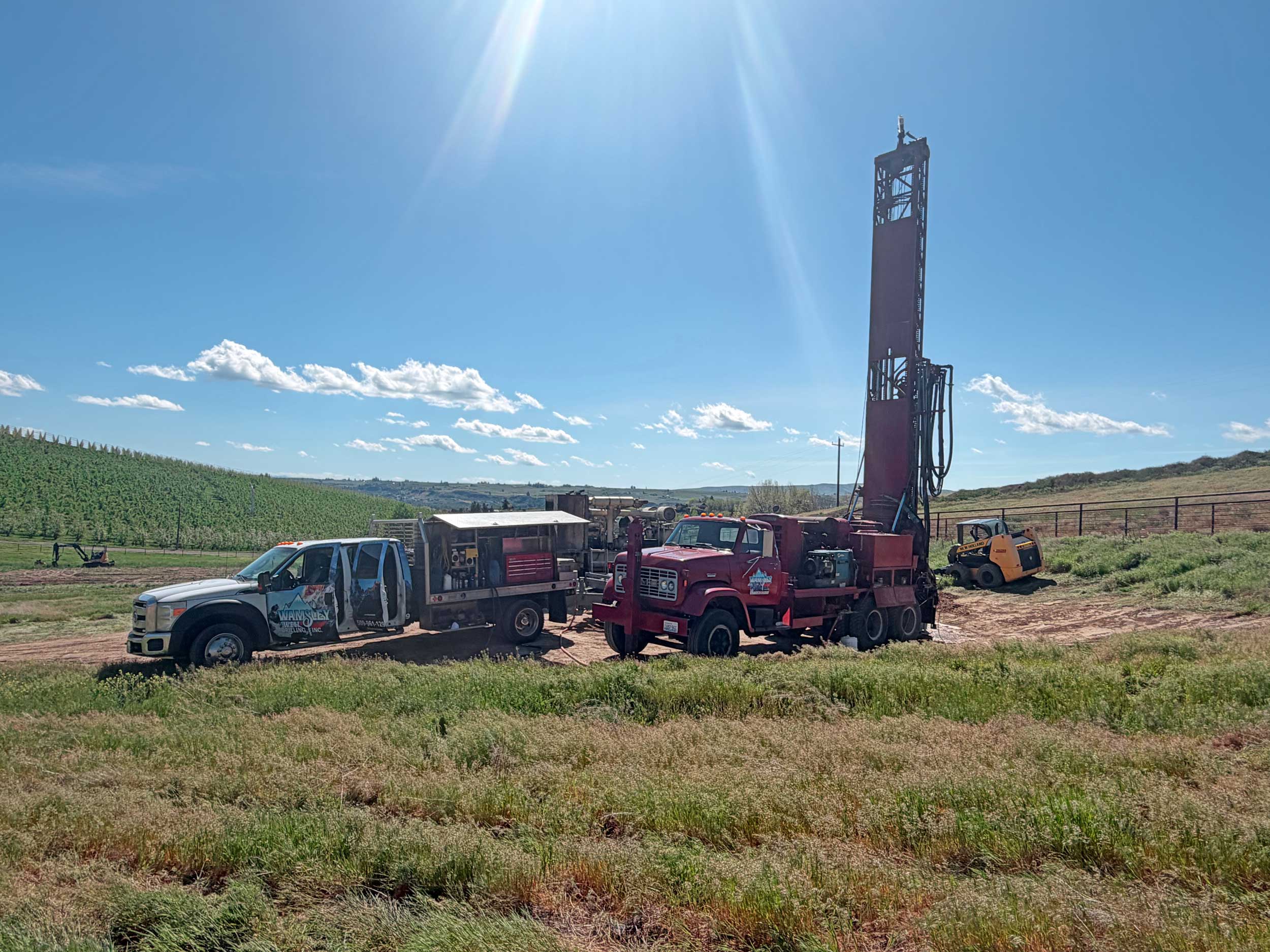 Wamsley Well Drilling Inc. well drilling rig and support trucks at a job site