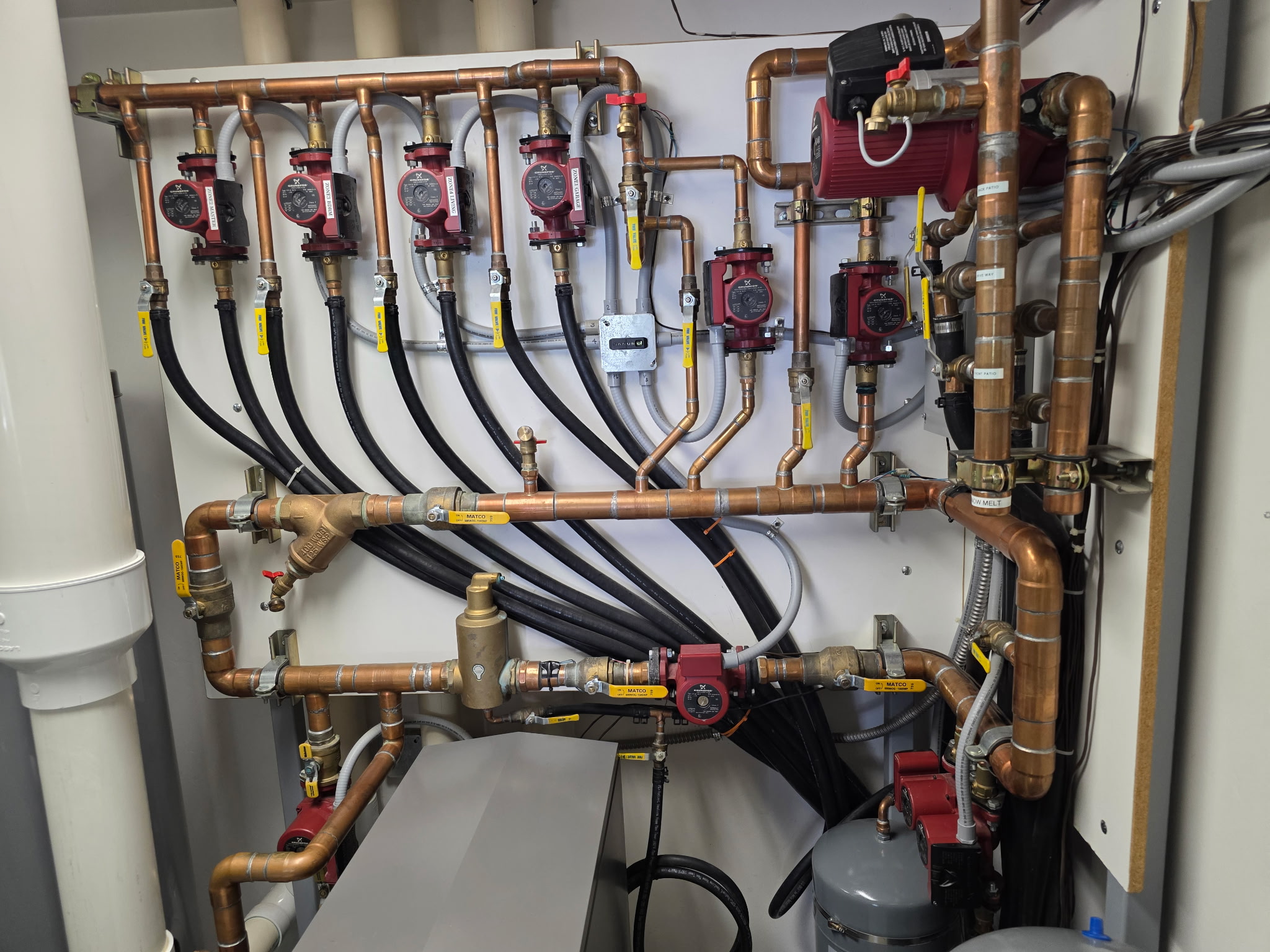 Sawtooth Plumbing & Heating Inc. plumbing and heating system with copper piping, valves, and circulator pumps inside a mechanical unit