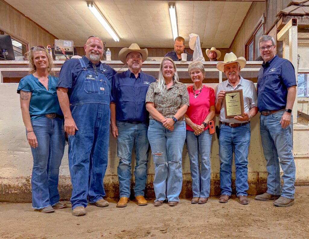 Group photo of Midwest Texas Longhorn Association members in cowboy attire holding an award certificate in a barn
